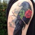 Tatuaje en el brazo, cuervo maravilloso realista con rosa en el pico que se siente en la rama