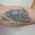 Inchiostro grigio che muove il vecchio tatuaggio commemorativo del treno a vapore sul bicipite con data