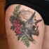 Illustrative style colored thigh tattoo of dinosaur skull
