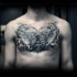 Large black ink chest tattoo of dinosaur skulls and human hand