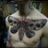 Large illustrative style chest tattoo of big butterfly stylized with human skulls