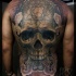 Large mystical looking whole back tattoo of big skull with ornaments and smoke