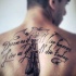 Tatuaje en la espalda, inscripción preciosa de letra cursiva y dos plumas, tinta negra