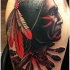 Tatuaje en el brazo, cara de indio oscuro con plumas en el cabello y flechas  con hacha