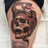 Old school style colored thigh tattoo of human skull stylized with evil snake