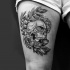 Tatuaje en el muslo, 
dibujo negro blanco de cráneo humano entre flores y hojas