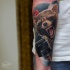 Realism style colored raccoon with fantasy gun tattoo on forearm