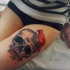 Simple colored thigh tattoo of human skull with red bird