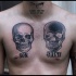 Small black and white chest tattoo of human skulls and lettering