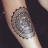 Stippling style black ink arm tattoo of circle shaped flower with lettering