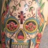 el tatuaje de una calavera mexicana con una cruz en sy frente hecho en el hombro con tinta de varios colores