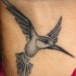 Tatuaje minimalista de un colibrí con alas abiertas.