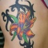 El tatuaje de un Lirio de color naranja y negro rodeado de unas hojas verdes y un entrelazado negro