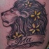 El tatuaje de la cabeza de un leon en perfil con flores de color amarillo en su melena y un palabra ma