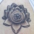el tatuaje de una flor de loto con una mantra om adentro hecho en color negro