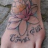 el tatuaje de una flor de loto lineada con unas letras en hindu hecho en el pie