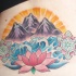 el tatuaje de una flor de loto, el mar y las montañas en el fondo hecho en color en la espalda