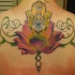 El tatuaje de flor de loto con el simbolo de la mano di fatima hecho en color en la espalda