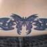 Tatuaje en bajo de la espalda, mariposa con tracería estilo tribal, color morado