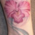 el tatuaje de una orquidea tierna de color rosa en la pierna