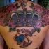 el tatuaje grande  muy colorado con una corona royal rodeada de flores rosas hecho en la espalda