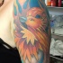 el tatuaje de la ave fenix de color naranja hecho en el hombro