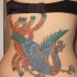 el tatuaje detallado y colorado de la ave magica fenix azul en la espalda