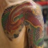 el tatuaje en estilo asiatico de una ave roja hecho en varios colores en el hombro y pecho