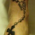 Tatuaje en tinta negra rosario con cruz en el tobillo