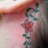 Tatuaje en color tracería floral detrás de la oreja