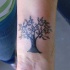 el tatuaje pequeño de una rbol con hojas hecho en color en la muñeca
