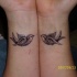 Tatuaje en la muñeca en tinta negra con  dos golondrinas