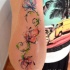Tender elegant colored flowers on vine forearm length tattoo by Javi Wolf in watercolor style