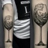 Schwimmender Wal im Wasser Wellen in Weinglas schwarzes und weißes Unterarm Tattoo im surrealistischen Stil