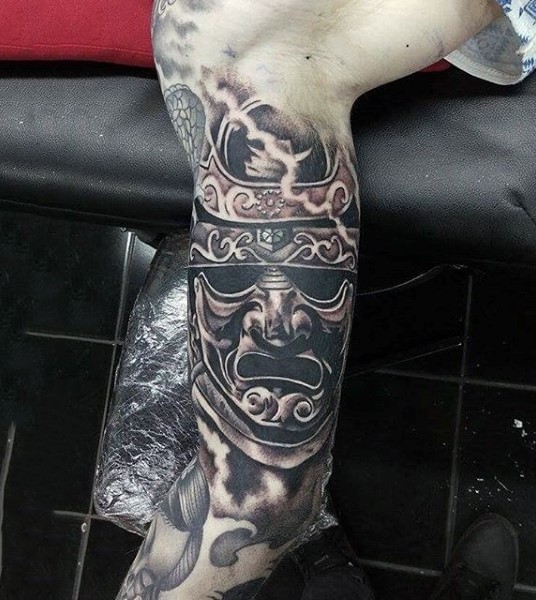 Tiny black and white mystical samurai helmet tattoo on upper arm