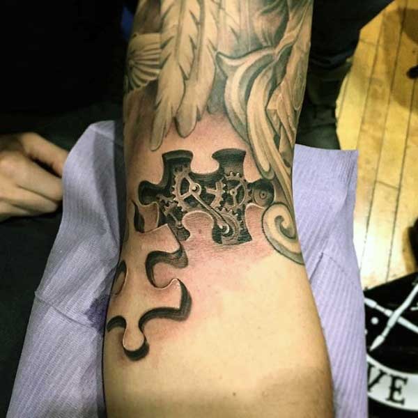 Tiny black ink 3D style puzzle piece tattoo on arm stylized with small mechanical parts