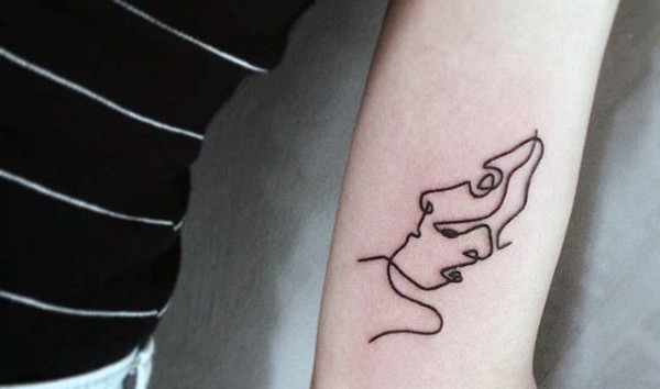 Tiny black ink simple portrait like tattoo on arm