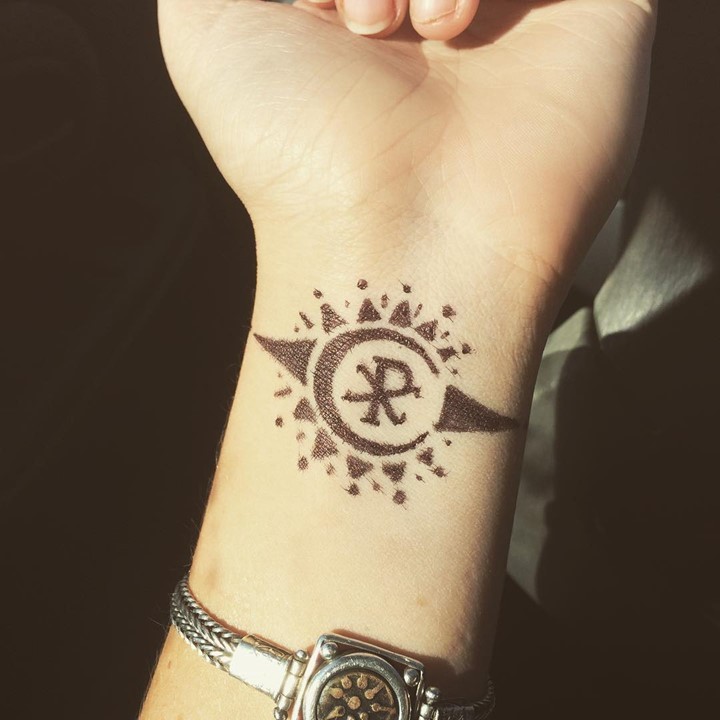 Tiny black ink wrist tattoo of sun shaped symbol