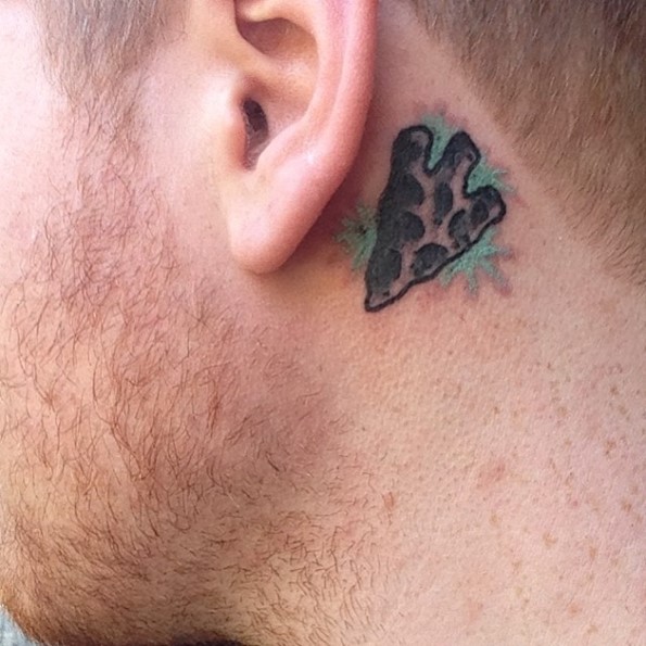 Tiny cartoon like colored behind ear tattoo of antic arrow head