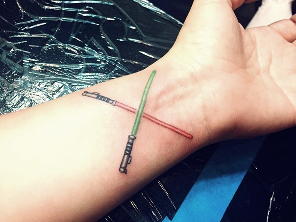 Winzige cartoonische farbige gekreuzte Lichtschwerter Tattoo am Handgelenk