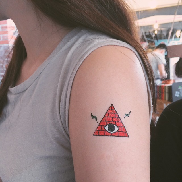 Tiny homemade like colored mystical pyramid with eye tattoo on upper arm