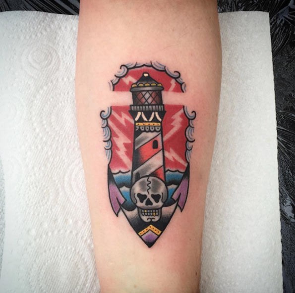 Tiny nautical style colored lighthouse tattoo on forearm with anchor stylized with skull