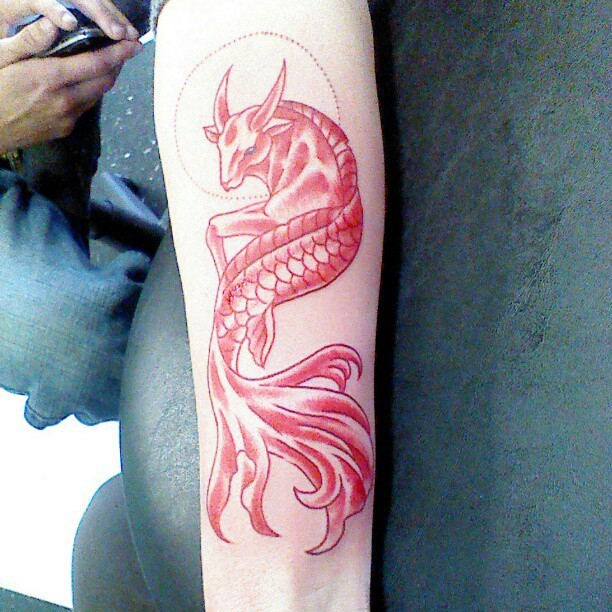 Tiny red colored fantasy Capricorn tattoo on forearm