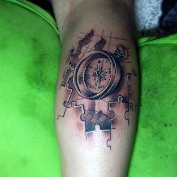 Typical black and gray style forearm tattoo of compass with puzzle pieces