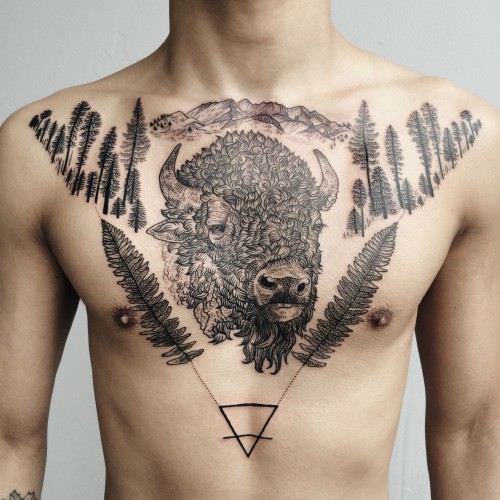 Typical black ink chest tattoo of wild aurochs with forest and mystic triangle