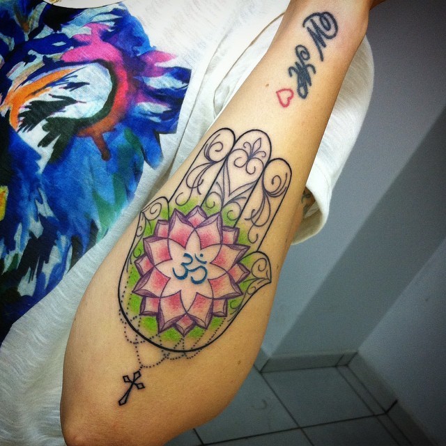 Typical illustrative style colored forearm tattoo of Hamsa symbol with cross