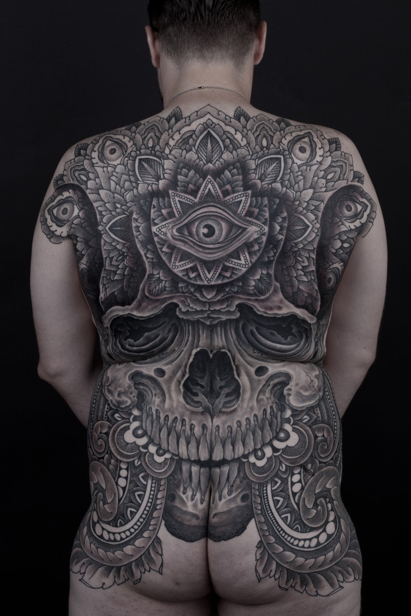 Typical large whole back tattoo of ancient human skull stylized with various ornaments and eye