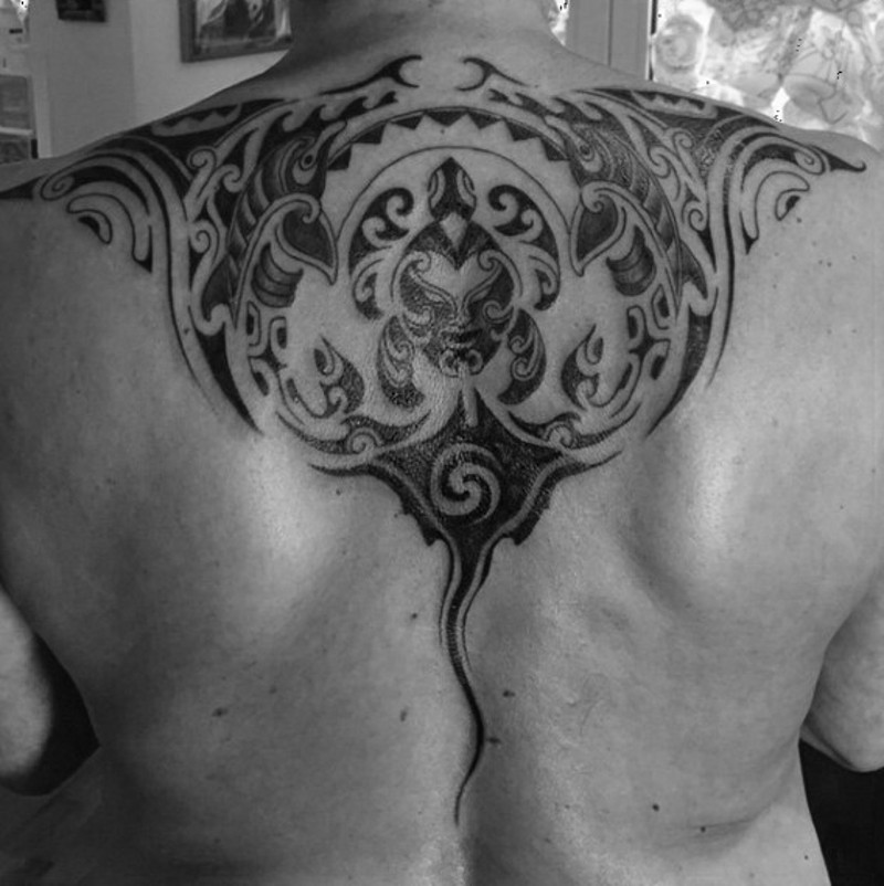 Unbelievable black ink ray tattoo on upper back stylized with Polynesian ornaments