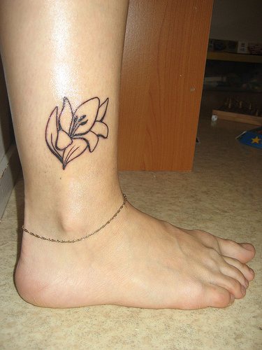 Uncolored opened flower ankle tattoo