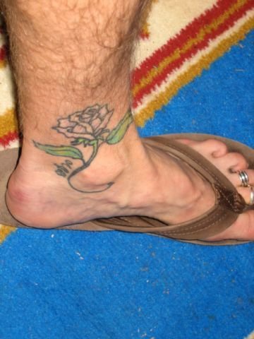 Uncolored rose with green leaves ankle tattoo
